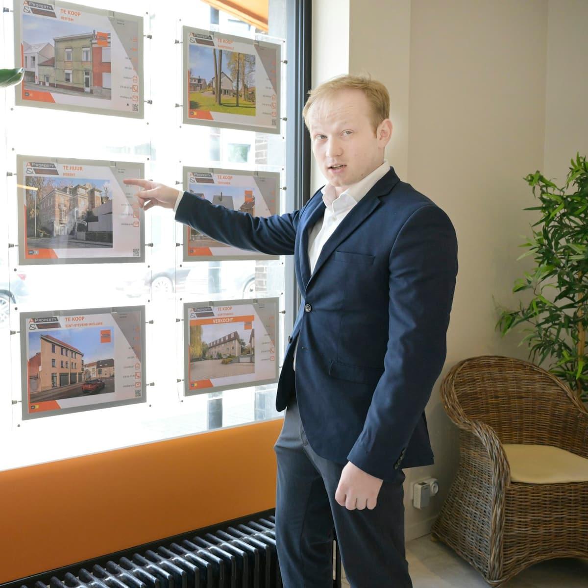 An estate agent at the window of a high-street agency, pointing at the property listings on display